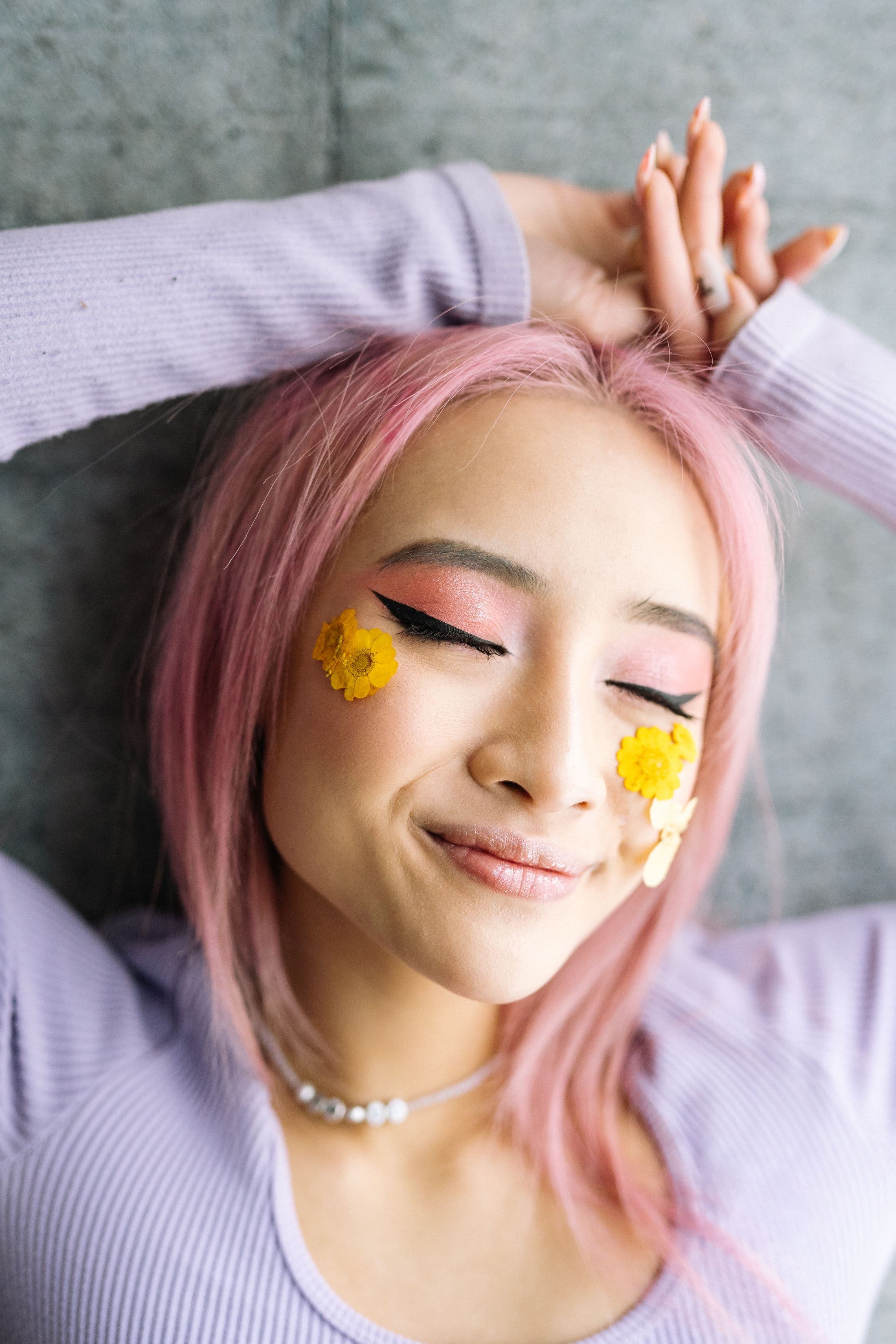 Lächelnde Frau mit rosa Haaren, pinkem Augen-Make-up und gelben Blüten auf den Wangen