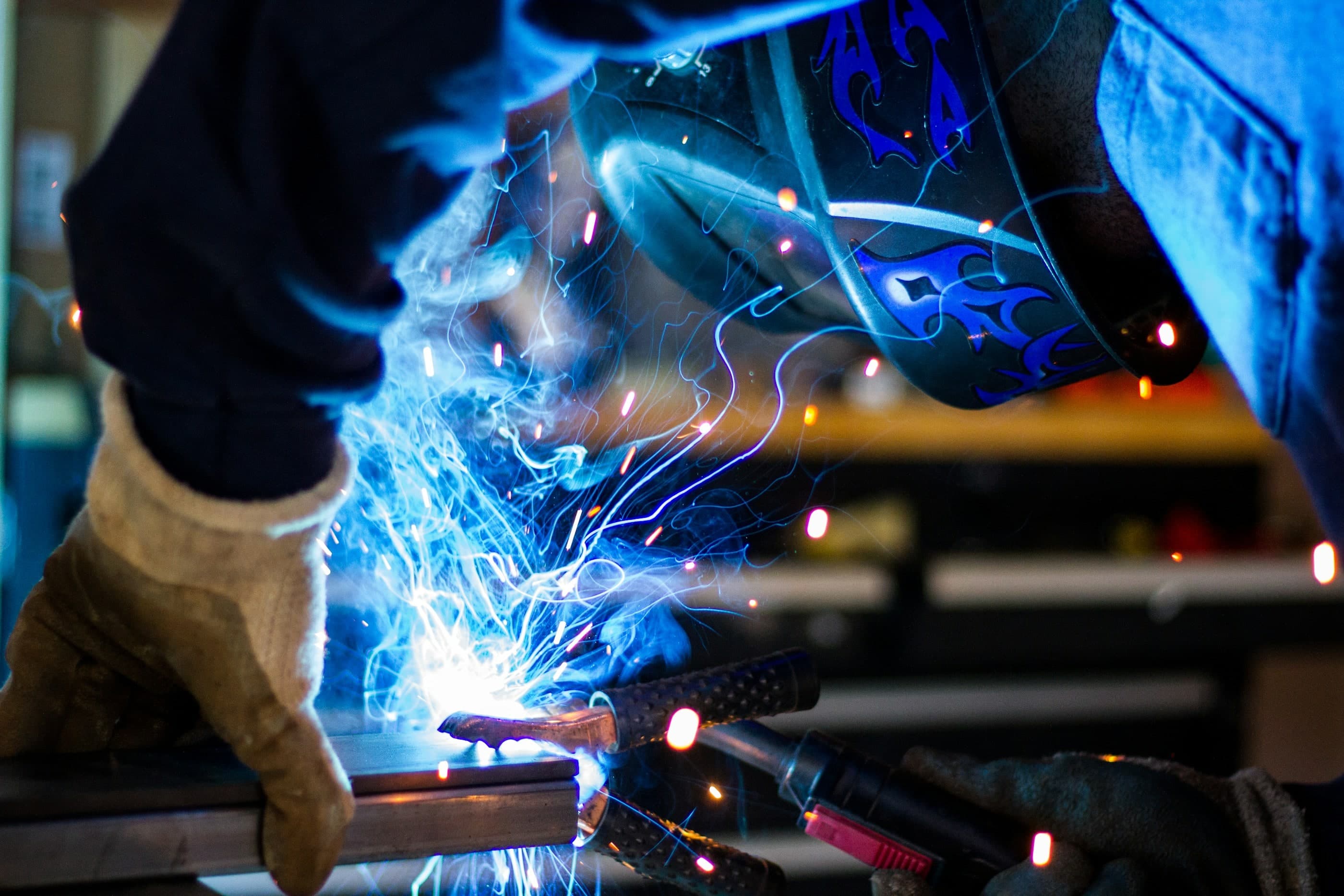 Ein Metallhandwerker mit Schutzhelm und Handschuhen beim Schweißen, umgeben von Funken