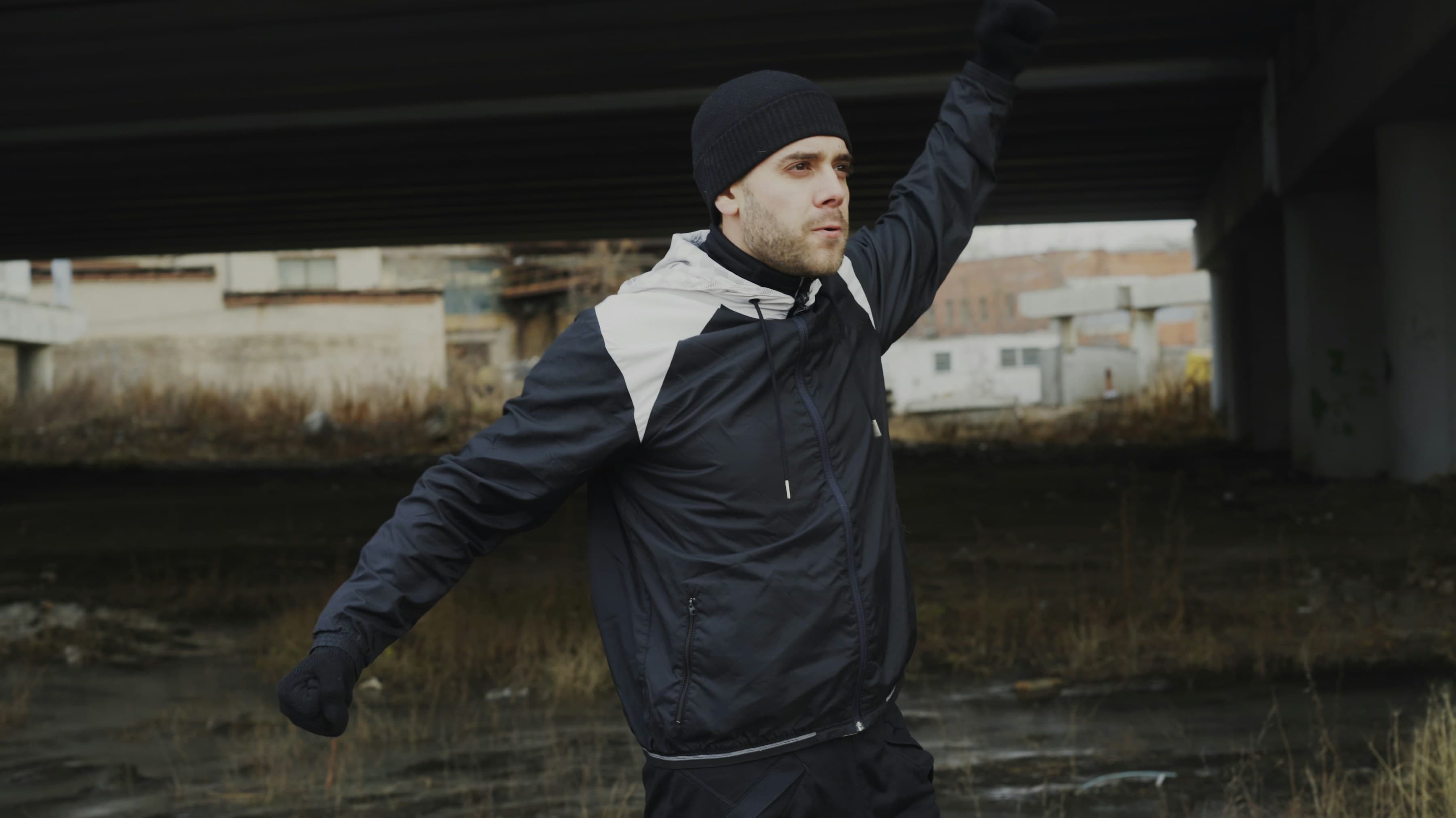 Athlet in dunkler Sportkleidung dehnt sich unter einer Brücke am Wasser