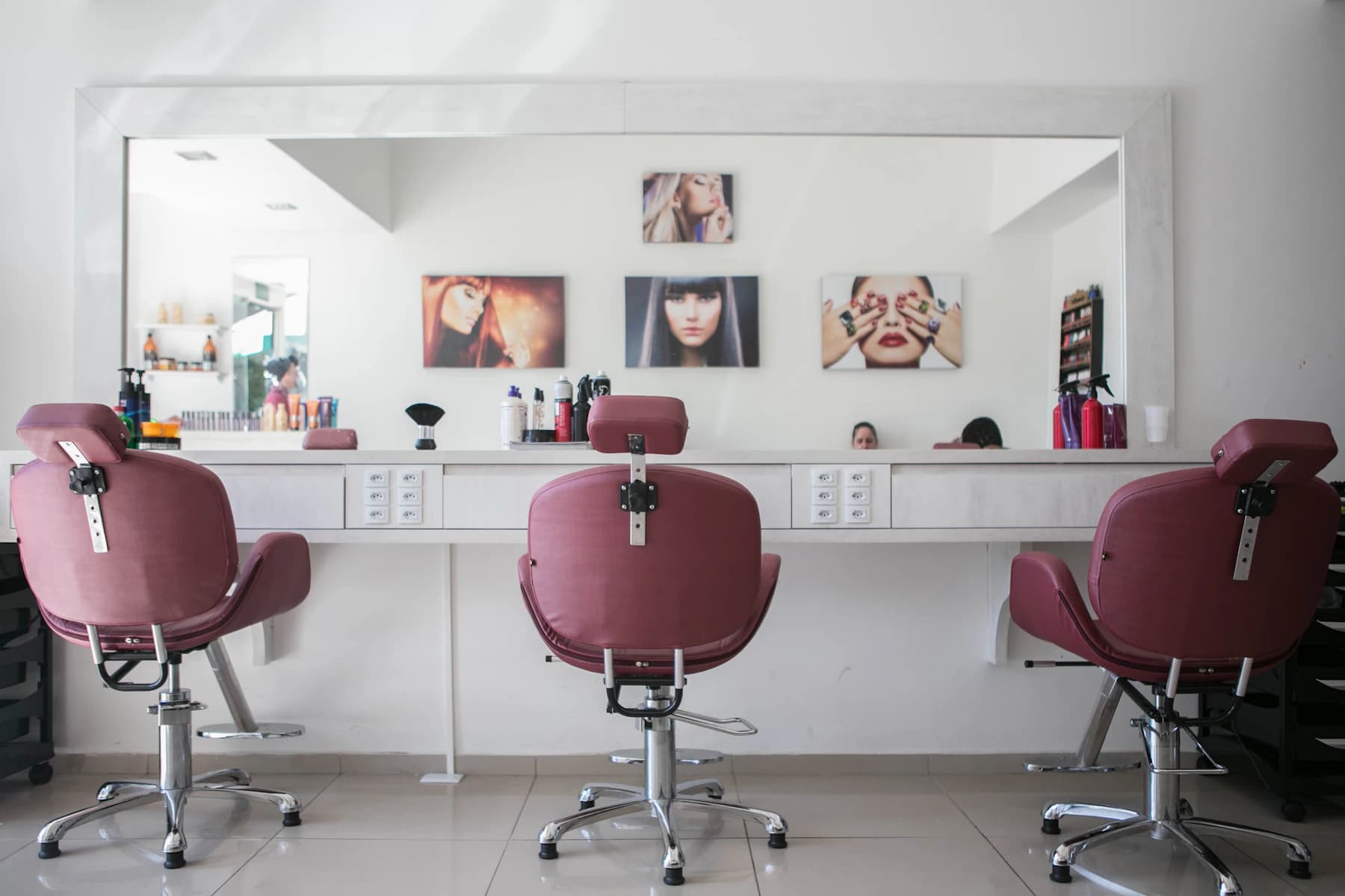 Heller Friseursalon mit großen Spiegeln und weinroten Salonstühlen